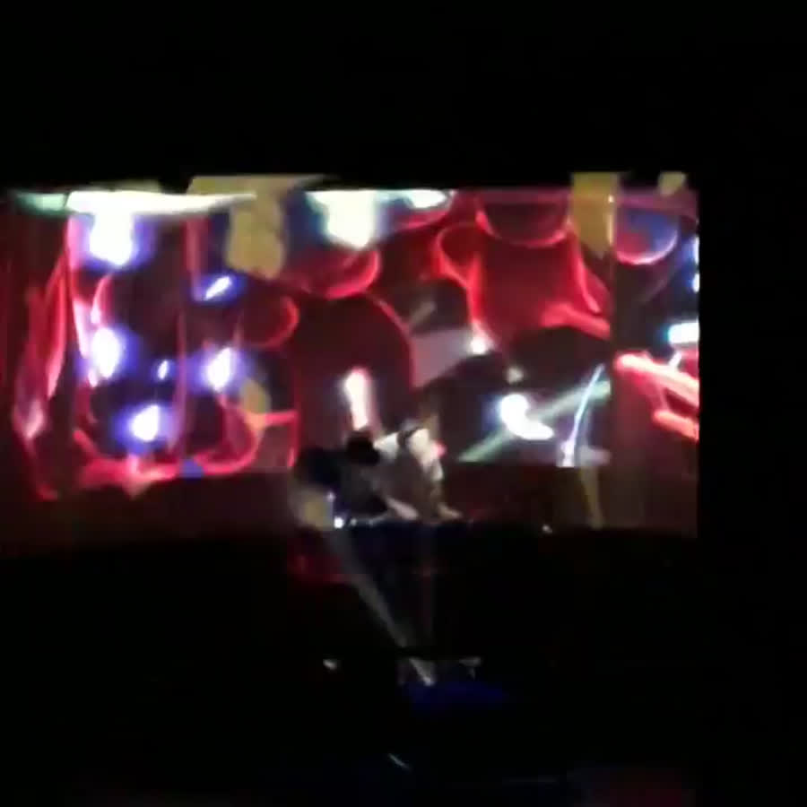 DJ Shadow on stage in front of a wide screen of red and blue neuron renders